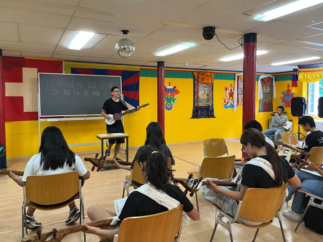 Tibetische Kinder und ihr Lehrer üben in einem Saal auf Musikinstrumenten.