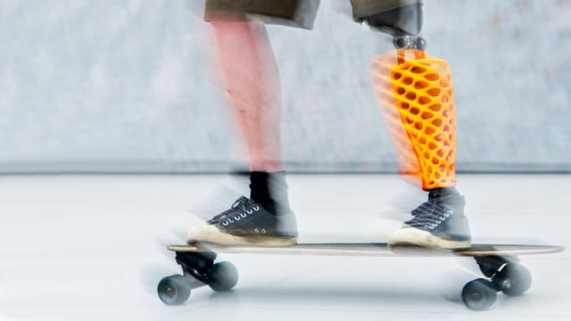 Ein Skateboarder mit oranger Beinprothese fährt Skateboard.