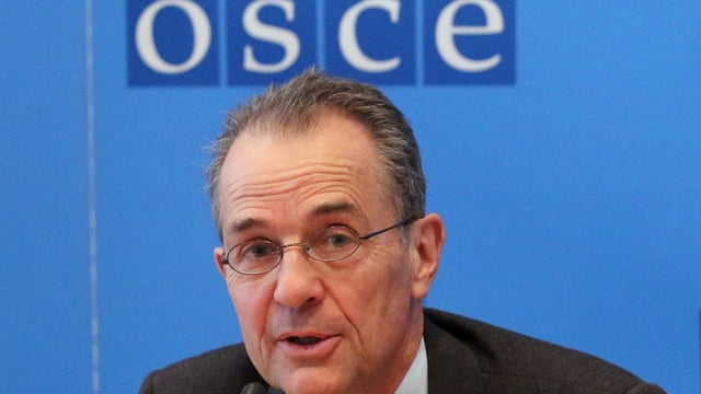 Ein Mann mit Brille vor dem OSCE-Emblem