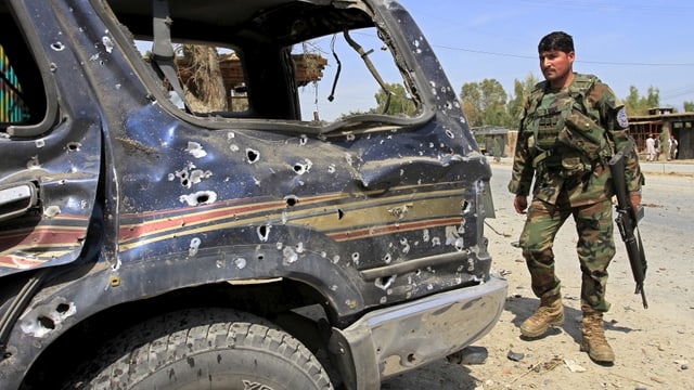 Ein afghanischer Soldat ohne Helm, mit Gewehr, steht hinter einem von Schüssen durchlöcherten Geländewagen.