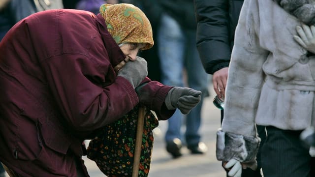 Alte Frau streckt ihre Hand für eine Spende aus.