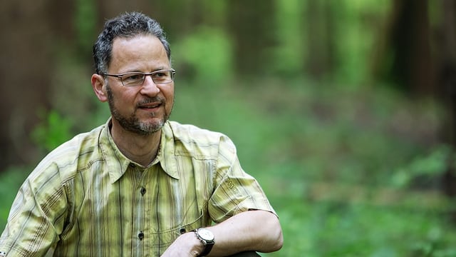 Ein Mann mittleren Alters mit zufriedenem Lächeln im Grünen.