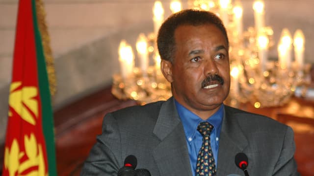 Der eritreische Staatspräsident Isayas Afewerki sitzt hinter Mikrofonen neben einer Fahne.