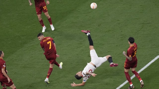 Ein Spieler mit weissem Trikot macht einen Fallrückzieher. Andere Spieler tragen ein rotes Trikot.