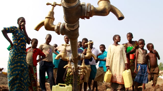 Symbolbild: Menschen – offensichtlich im ländlichen Afrika – stehen um einen Wasserhahn herum.