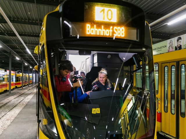 Eine Tramfahrerin sitz im Führerstand und spricht ins Mikrofon.