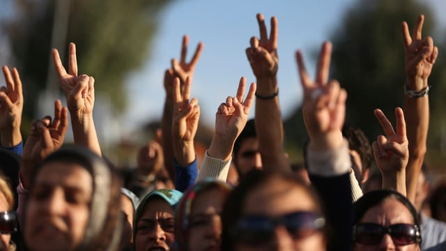 Ein Demonstrationszug in Nahaufnahme, die Menschen strecken ihre Arme hoch und machen mit Zeige- und Mittelfinger das Victory-Zeichen.