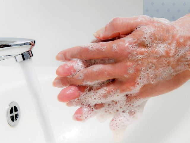 Hände voller Seife vor Wasserhahn