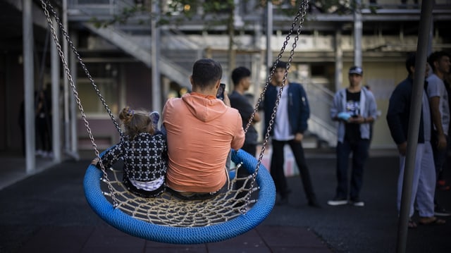 Ein Mann telefoniert auf einer Schaukel. 