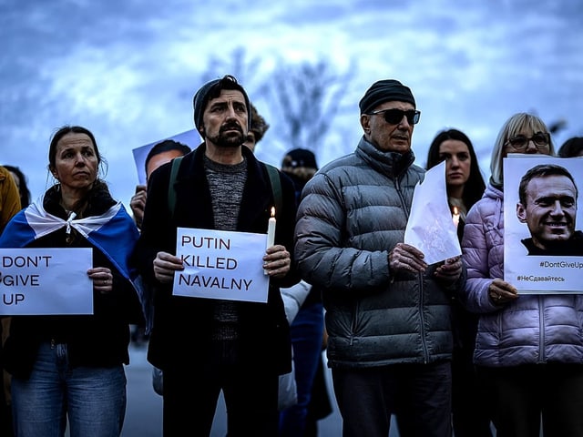 Menschen halten Kerzen und Plakate mit der Aufschrift "Putin hat Nawalny getötet" und Porträts Alexey Nawalnys.