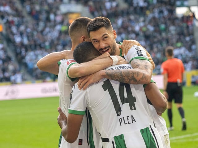 Fussballspieler feiern auf dem Spielfeld eine Umarmung.