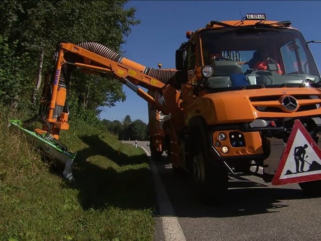 Strasse mit grossem Mähfahrzeug. mäht Grasfläche