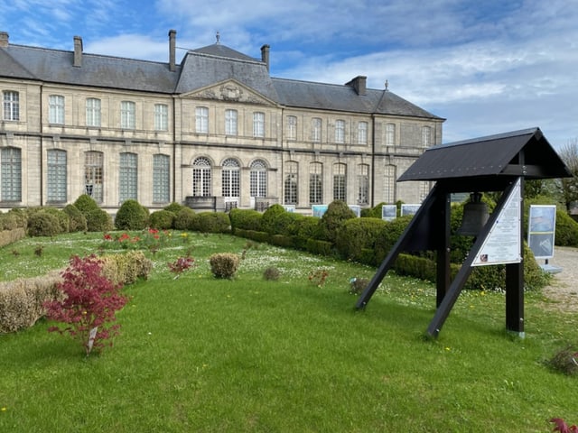 Historisches Gebäude mit gepflegtem Garten und Schautafeln.