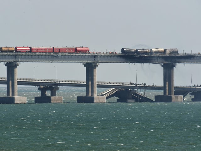 Ein demolierter Güterzug steht auf der teils zerstörten Brücke.