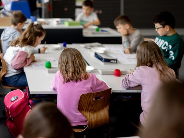 Schüler sitzen an Tischen und arbeiten in einem Klassenzimmer.