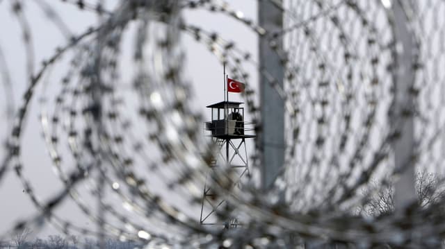 Ein Drahtzaun, im Hintergrund ein Turm mit türkischer Flagge