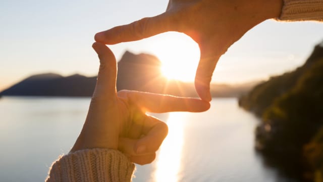 eine Person formt mit den Händen ein Viereck im Sonnenuntergang