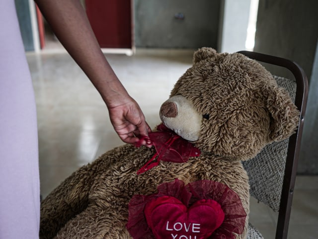 Person gibt einem Teddybär ein rotes Herz mit Aufschrift 'LOVE YOU'.