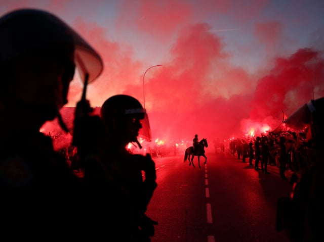 Polizisten mit Visier, einer auf einem Pferd, rote Nebelschwaden. Es ist fast dunkel. 