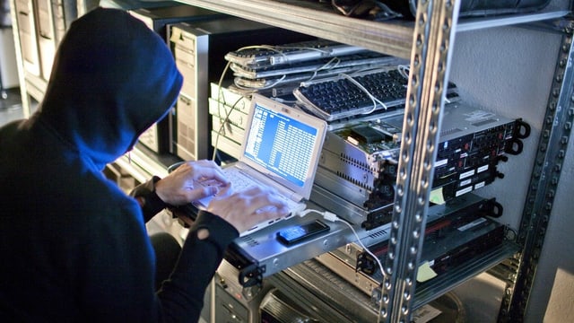 Symbolic image, a hacker is sitting at a computer and programming codes.