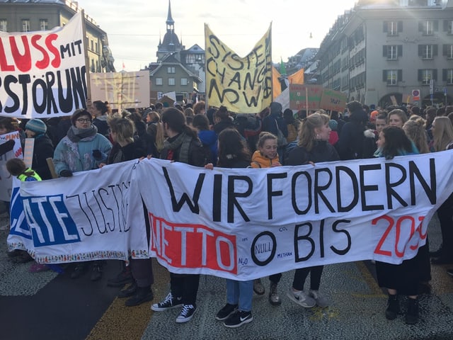 Menschenmenge auf grossem Platz. Die Menschen halten verschiedene Plakate und Transparente.