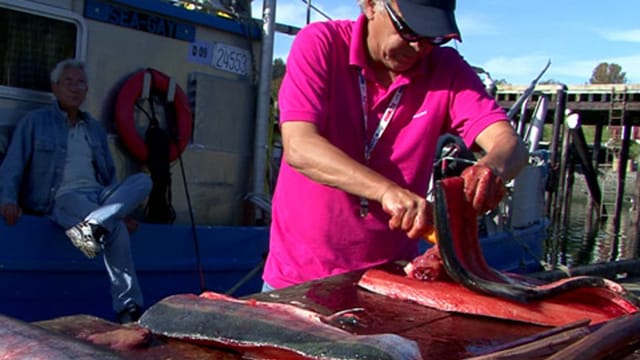 Ein Mann schneidet filetiert einen Lachs am Hafen.