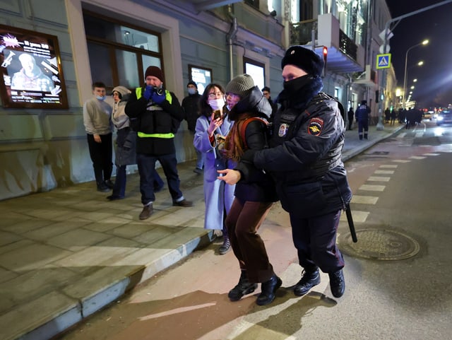 Ein Polizist führt eine Frau auf der Strasse ab. Passanten schauen zu.