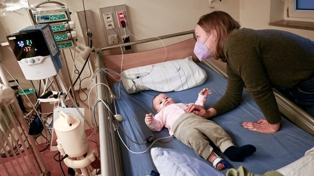 Eine Mutter beugt sich über das Krankenbett ihres Babys.