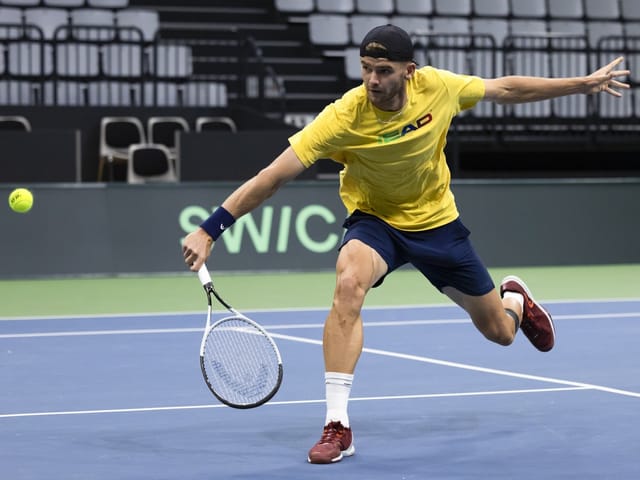 Tennisspieler streckt sich nach einem Ball auf dem Platz.