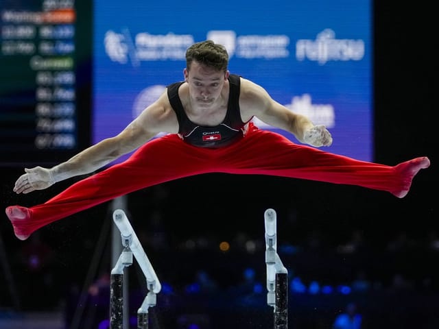 Turner springt über Parallelschinen im Wettkampf.