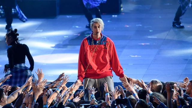 Justin Bieber auf der Bühne vor ausgestreckten Armen seiner Fans an einem Konzert.