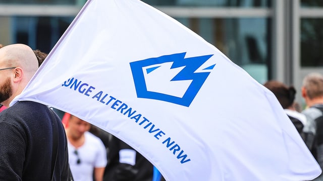 Mann mit Glatze hält weisse Flagge mit Logo der Jungen Alternativen