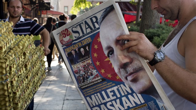 Ein Mann, rechts, liest an einer belebten Strasse eine türkische Zeitung mit Erdogan auf der Titelseite.