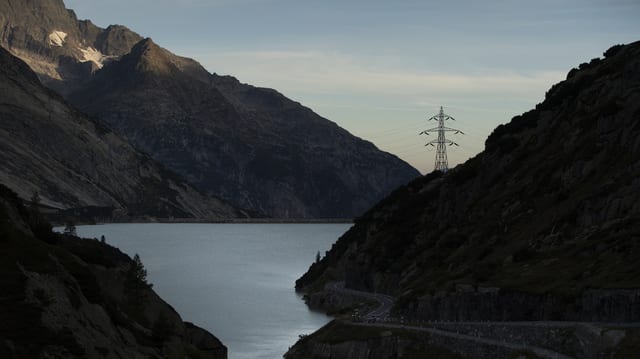 Ein Stausee in den Bergen, in der Ferne ein Strommast.