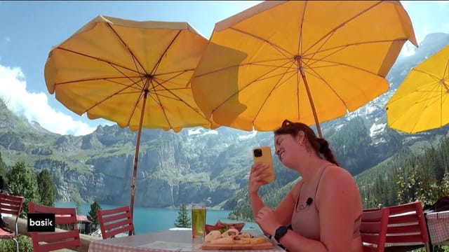 Roxanne im Restaurant oberhalb des Oeschinensees unter einem gelben Sonnenschirm. Sie macht am Tisch sitzend ein Selfie.