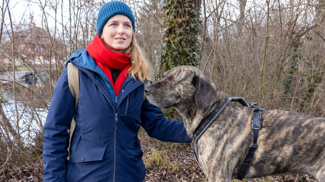 Frau mit Schal und Kappe neben ihrem Hund.