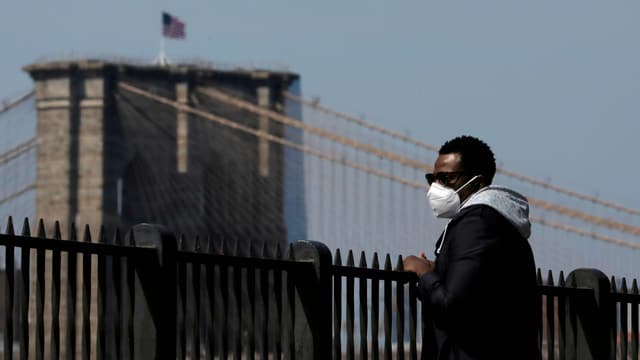 The man in a mask looks at the Brooklyn Bridge.