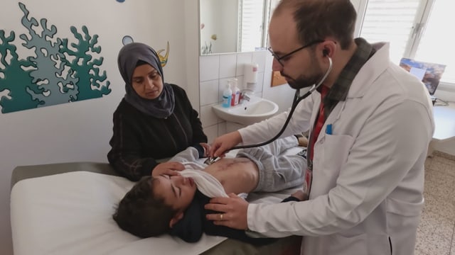 Naeem und seine Mutter sind im Kinderspital. Ein Arzt hört mit einem Stethoskop den Herzschlag ab.