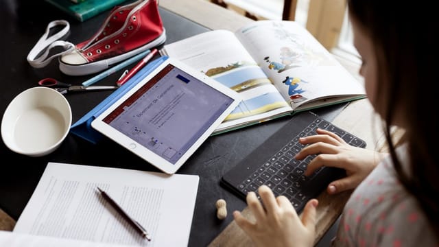 Ein Kind macht Hausaufgaben, mit Büchern und Tablet-Computer.