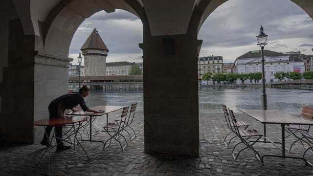 Woman cleans tables. Behind you can see the Chapel Bridge.