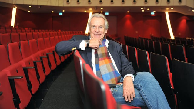 Pepe Lienhard sitzt auf Stuhl in leerem Theatersaal.