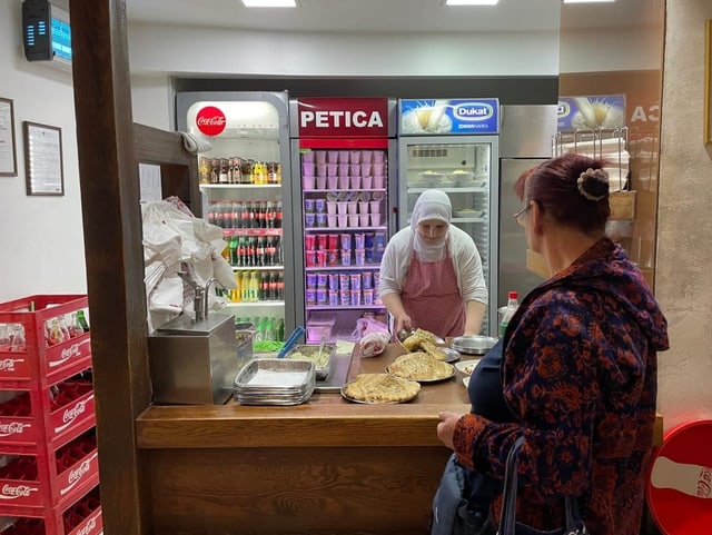 Eine Frau bereitet für eine Kundin Cevapi vor.