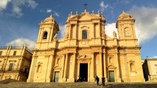 Eine grosse gelbliche Kathedrale mit Statuen, Säulen und Türmen. 