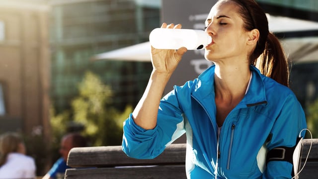 Joggerin erfrischt sich mit einem Schluck aus einer Sportflasche.