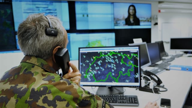 Telefonierender Mann am Computer. Vor sich auf dem Bildschirm eine Schweizer Karte.