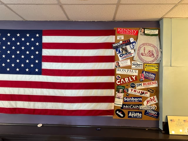 US-Flagge, daneben kleben Sticker mit den Namen der Ex-Kandidierenden.