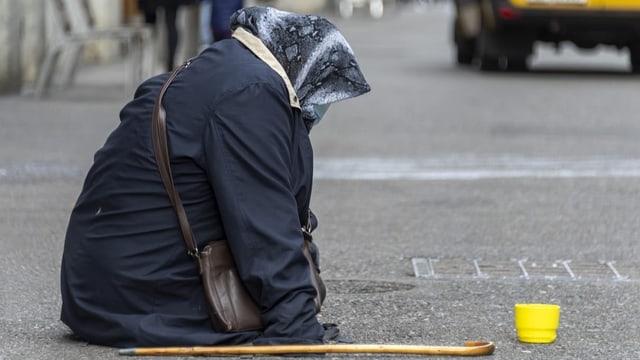 eine Frau mit Kopftuch bettelt auf der Strasse