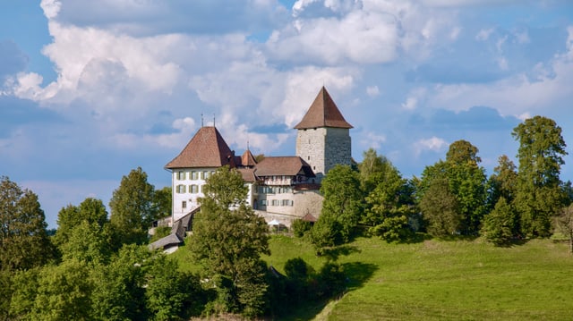 Ein malersiches Schloss bei schönem Wetter umgrünt auf einem Hügel.