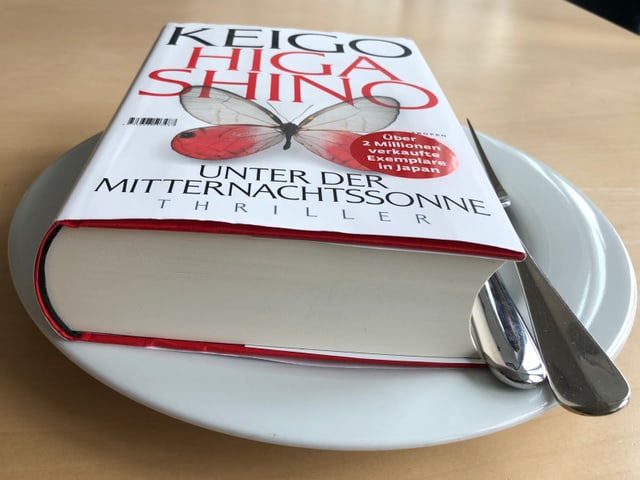 Das Buch «Unter der Mitternachtssonne» liegt auf einem weissen Teller. Messer und Gabel daneben.