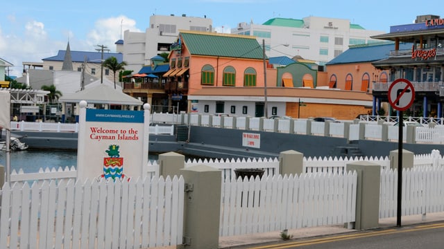 Anlegestelle auf den Cayman Inseln mit einem Willkommensschild, weisse Zäune und Hotels.